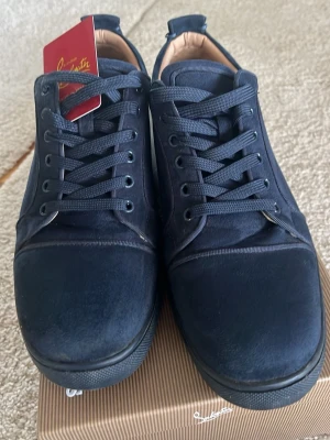 Mörkblå sammetssneakers Louboutin - Snygga mörkblå sneakers från Christian Louboutin i sammet med klassisk röd sula. Lågt skaft, rund tå och svarta snören. Perfekta för dig som vill sticka ut med exklusiva detaljer och lyxig känsla. Kommer med originalkartong.