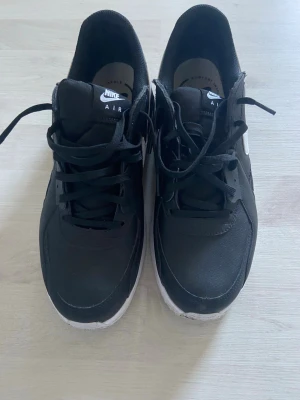Svarta Nike Air sneakers - Svarta Nike Air sneakers med vit sula och klassisk logga på både plös och häl. Skorna har lågt skaft, snörning och är tillverkade i syntetmaterial och textil. Perfekta för en sportig och stilren look. Använd fåtal gånger då jag testat skorna. Pris kan diskuteras privat!