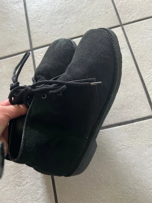 Svarta mockakängor med snörning storlek 40 från Bird - Säljer ett par stilrena svarta kängor i mocka med klassisk snörning och rundad tå. Skorna har en låg sula och enkel design som passar till många olika outfits. Perfekta för dig som gillar en clean och tidlös look.