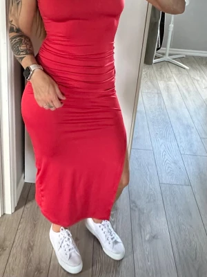 Hallonröd långklänning med slits - Snygg hallonröd långklänning i figurnära modell med slits på sidan. Klänningen är ärmlös och har en enkel, stilren design som framhäver siluetten. Perfekt för dig som vill ha en klänning som sticker ut och känns bekväm. Öppen rygg. Strl S. Använd en gång. 