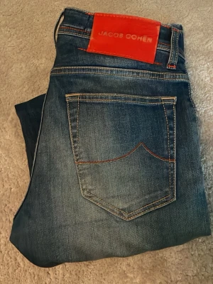 Blå jeans från Jacob Cohen - Snygga blå jeans från Jacob Cohen. Jeansen har en röd patch med logga bak i midjan och är tillverkade i mjukt denimtyg. 