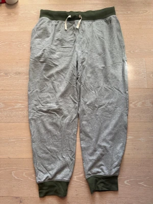 Grå mjukisbyxor från Polo Ralph Lauren - Grå mjukisbyxor från Polo Ralph Lauren med gröna muddar och midja samt dragsko. Klassisk broderad logga i grönt på ena benet. Sköna och avslappnade med resår i benslut. Perfekta för chill eller träning.