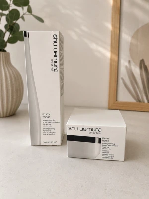 Shu Uemura Izumi Tonic hårvård - Shu Uemura Izumi Tonic strengthening treatment system för skört hår. Innehåller schampo och hårinpackning med risvatten. Förpackningarna är vita med svarta detaljer och minimalistisk design. Perfekt för dig som vill stärka och vårda håret.