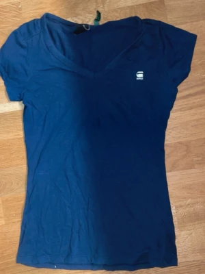 Mörkblå v-ringad t-shirt G-Star RAW - Säljer en mörkblå v-ringad t-shirt från G-Star RAW. T-shirten har korta ärmar och en liten logga på bröstet. Tillverkad i mjuk bomull som känns skön mot huden. Perfekt till jeans eller shorts för en enkel och clean look. Storlek XS 