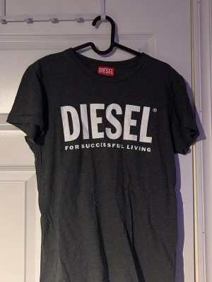 Mörkgrå t-shirt från Diesel - Snygg mörkgrå t-shirt från Diesel med stort vitt logotryck på bröstet. Klassisk passform med rund halsringning och korta ärmar. Perfekt för en avslappnad och trendig stil.