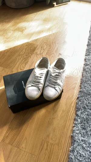 Vita Saint Laurent sneakers med leoparddetalj - Snygga vita sneakers från Saint Laurent med klassisk låg profil och leopardmönstrad detalj på hälen. Skorna har vita snören och sula i gummi. Perfekta för dig som vill ha en stilren men ändå unik look. Storlek 40 passar 41 