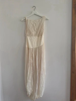 Helt ny lång klänning från Zara - Lång vit klänning från Zara i ett lätt, crinklat tyg. Klänningen har breda axelband och markerad midja som ger en snygg siluett. Perfekt för sommarens alla tillfällen och enkel att styla med accessoarer. Prislapp fortfarande kvar.