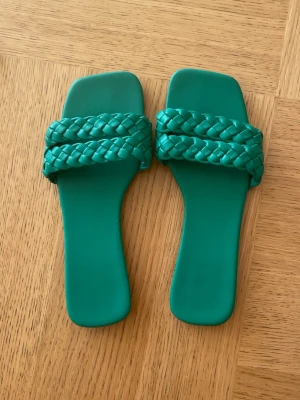 Gröna flätade sandaler med fyrkantig tå - Säljer ett par trendiga gröna sandaler med breda flätade remmar och fyrkantig tå. Sandalerna har en stilren design och är tillverkade i ett slätt, syntetiskt material. Perfekta för dig som vill sticka ut med färg och form.