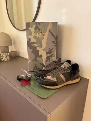 Valentino Rockrunners - Snygga sneakers från Valentino Garavani med grått och grönt camomönster, svarta detaljer och beige sula. Skorna har mesh och mocka-paneler samt klassisk snörning. Kommer med originalkartong, extra skosnören och dustbag.