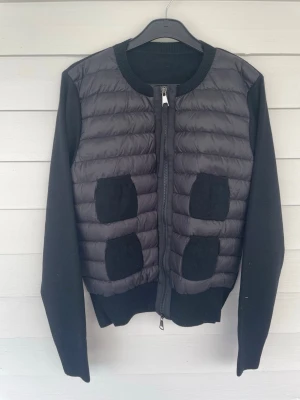 Svart quiltad cardigan med fickor - Snygg svart cardiganjacka med quiltad framsida och stickade ärmar. Fyra stickade fickor framtill och dragkedja hela vägen. Rund halsringning och ribbade muddar. Perfekt för lager på lager och en cool streetstyle-look.