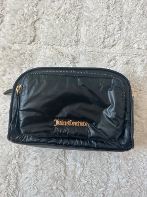 Svart Juicy Couture handväska - Snygg svart handväska från Juicy Couture i glansigt material med guldfärgade detaljer och dragkedja!! Tyvärr saknar banden till väskan💕💕