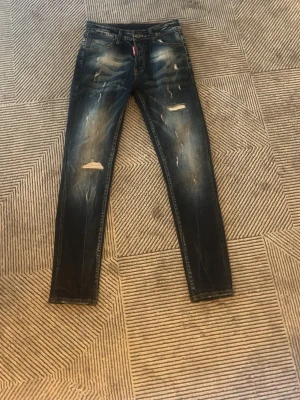 Mörkblå slitna jeans Dsquared2 - Snygga mörkblå jeans från Dsquared2 med slitningar och trasiga detaljer på benen. Klassisk femficksmodell med smal passform och cool tvätt. Perfekta för dig som gillar en trendig och avslappnad stil.