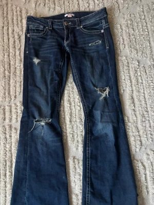 Mörkblå bootcut jeans med slitningar - Snygga mörkblå bootcut jeans från Only med slitna detaljer och hål på benen. Jeansen har klassisk femficksdesign, låg midja och kontrastsömmar. Perfekta för en avslappnad och trendig look.