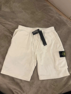 Vita shorts från Stone Island - Snygga vita shorts från Stone Island med elastisk midja och en praktisk ficka på sidan med den klassiska loggan. Perfekta för sommaren och har en clean look som passar till det mesta.