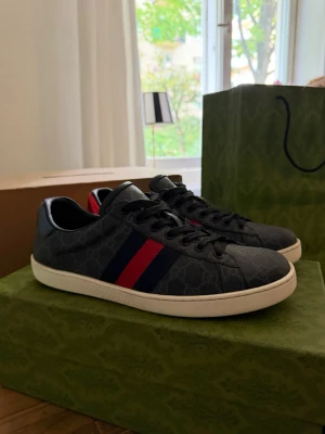 Gucci Ace - Snygga svarta Gucci sneakers med klassiskt GG-monogram i grått och ikoniska röda och mörkblå ränder på sidorna. Skorna är i storlek 43 men gymmet kvalitet samt skick skorna är använda få tal gånger!