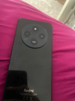 Svart Redmi mobiltelefon med trippelkamera - Säljer en svart Redmi smartphone med stilren design och rund kameramodul på baksidan. Mobilen har trippelkamera med 50MP huvudkamera och en stor skärm med droppformad sensor. Baksidan är blank och tillverkad i glasliknande material.