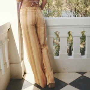 Beige randiga linnebyxor - Säljer ett par beige linnebyxor med tunna vertikala ränder i ljusa toner. Byxorna har hög midja och vida ben för en avslappnad och trendig look. Perfekta för sommardagar och ger en skön, luftig känsla. Inget synligt märke.