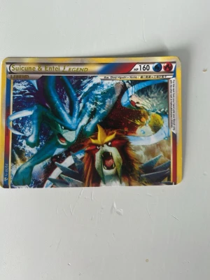 Pokémonkort Suicune & Entei LEGEND - Säljer ett samlarkort från Pokémon med motiv av Suicune och Entei från LEGEND-serien. Kortet har färgstark design med blå, röd och gul ram och detaljer. Perfekt för dig som gillar Pokémon eller samlar på unika kort.
