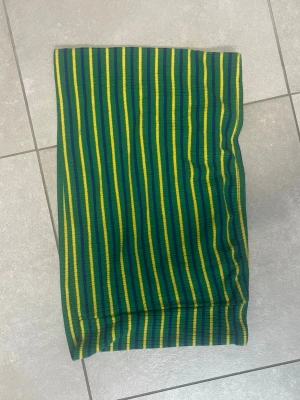 Randig ribbad tubtopp i gröny, gult och blå - Färgglad tubtopp med gröna, gula och blå ränder. Toppen är ribbad och har en tight passform som sitter snyggt. Perfekt för sommaren och enkel att matcha med både kjol och jeans. Den är kort och super för varma dagar. 