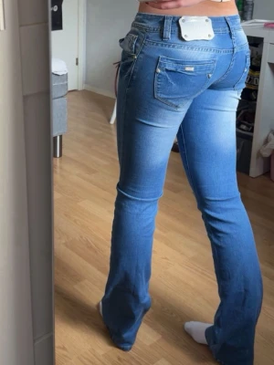 Lågmidjade bootcut blå jeans - Så snygga jeans från goodies jeans. De har en svag gräsfläck på ena benet som säkert går bort i tvätten. Märket där bak har lossat lite men sitter kvar! Storlek 40 men passar mindre med. Är 172cm ish