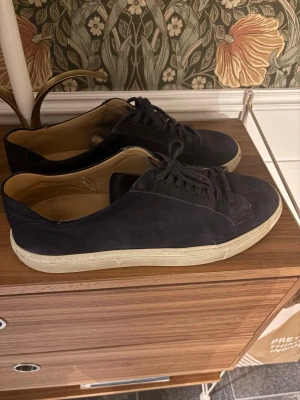 Mörkblå sneakers i mocka - Stilrena Mörkblåa sneakers i mocka med vit sula och klassisk låg profil. Skorna har mörkblåa skosnören och en insida i ljust läder. Perfekta för dig som gillar en clean och enkel look.