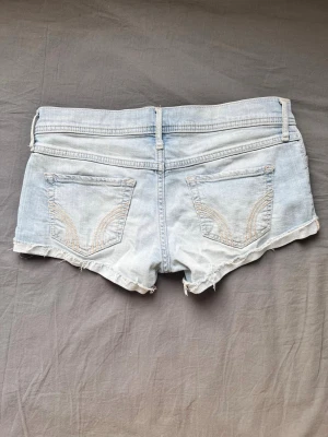 Ljusblå jeansshorts med fransig kant - Snygga ljusblå jeansshorts med fransig, rå kant och klassiska fem fickor. Shortsen har bälteshällor och knappstängning framtill. Perfekta för varma dagar och en avslappnad stil. Midjemått 78cm