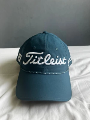 Mörkblå Titleist keps - Golfkeps använd runt 2-3 gånger. Snygg mörkblå keps från Titleist med broderad logga framtill och texten PRO V1 på sidan. Klassisk böjd skärm och ventilerande hål upptill. Onesize men justerbar.