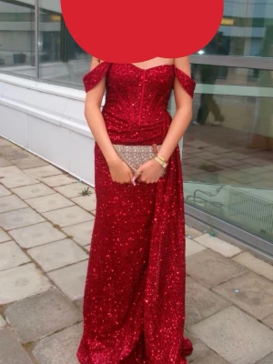 Röd glittrig balklänning med offshoulder - Säljer en fantastisk röd långklänning med glittrigt tyg och offshoulder-band. Klänningen har figurnära passform upptill, markerad midja och långa linjer som ger en elegant siluett. Perfekt för bal eller festliga tillfällen. (Använt en gång)