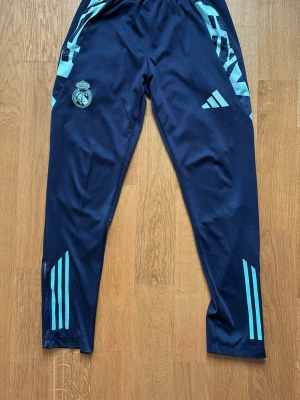 Real Madrid träningsbyxor Adidas - Mörkblå träningsbyxor från Adidas med Real Madrid-logga på. Byxorna är i ganska bra skick med ett jätte litet hål som man typ inte ser. Skriv om du undrar något👍