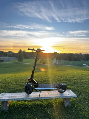 Kukirin M4 Max - Elektrisk scooter i svart med breda däck och robust ram. Scootern har röda detaljer vid bakhjulet, ståplatta i metall och raka handtag. Perfekt för smidig transport och enkel att ladda. Märket syns inte tydligt på bilderna.