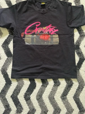 Corteiz t-shirt - Svart t-shirt från  Corteiz med färgstarkt tryck framtill i rosa och rött, föreställande graffiti och en digital klocka. Klassisk passform och rund halsringning. Perfekt för dig som gillar streetwear och unika prints.passar även S