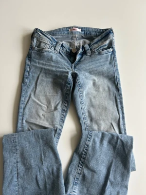 Ljusblå jeans från Gina Tricot - Säljer ett par ljusblå jeans från Gina Tricot i storlek XS. Rosa detaljer på baksidan. Väldigt fina och lågmidjade, nästan aldrig använda.