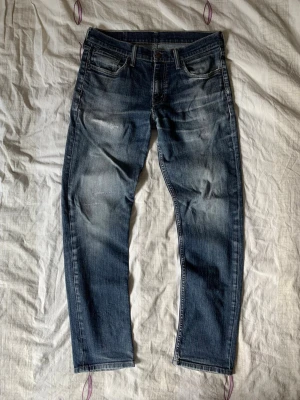 Levis jeans - Säljer ett par blå jeans med snygga slitningar och raka ben. Jeansen har klassisk femficksdesign och en cool tvättad look. Perfekta för dig som gillar en avslappnad och trendig stil. Materialet är denim i bomull.