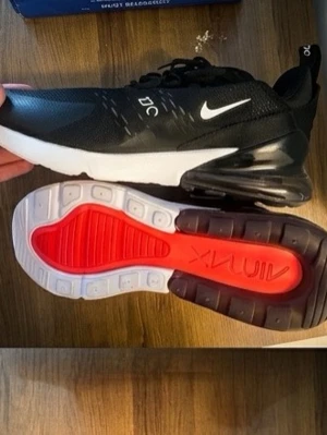 Nike Air Max 270 svarta sneakers - Nike Air Max 270 sneakers i svart dock ingen sula och synlig Air Max-dämpning i hälen. Ovandelen är i mesh för bra andningsförmåga och har vita detaljer som Swoosh-loggan och 270-tryck. Sulan har en röd detalj undertill. Perfekta för en sportig och trendig look.