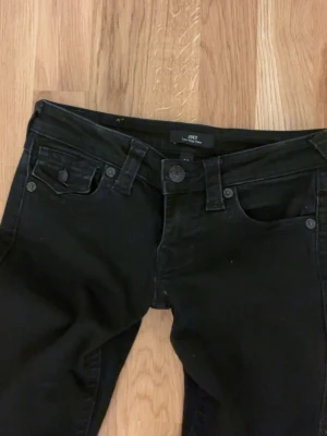 Svarta bootcut jeans från JOEY - Svarta jeans från JOEY med bootcut passform och klassisk femficksdesign. Jeansen har normal midja och är tillverkade i ett stretchigt denimtyg som ger en snygg siluett. Perfekta för dig som gillar en tidlös och trendig look.