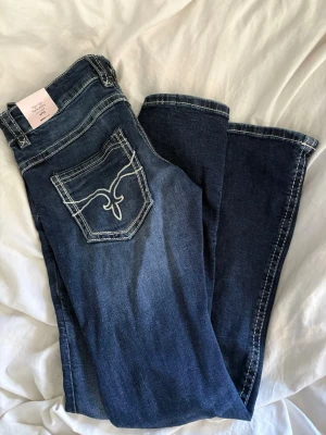 Blå flare jeans från Gina Tricot - Säljer ett par blå low rise flare jeans från Gina Tricot med snygga vita kontrastsömmar och broderad bakficka. Jeansen har ultra låg midja och utsvängda ben. Super sköna och aldrig använda. Prislapp kvar🥰 Köpta för 500 kr! Lite stora för mig som vanligtvis har 34-36, ungefär S.