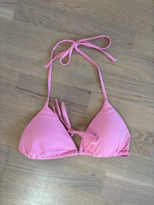 Rosa trekantsbikini med knyt - Söt rosa trekantsbikini med knyt i nacken och ryggen. Klassisk modell som ger en enkel och fräsch look på stranden. Perfekt för soliga dagar och lata timmar vid poolen. Köptes 2025 och är nytvättad💞