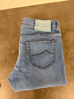 Ljusblå jeans från Jacob Cohën W35 - Snygga ljusblå jeans från Jacob Cohën med klassisk femficksmodell och raka ben. Jeansen har en stilren bakficka med kontrastsöm och ett blåvitt märke i midjan. Tillverkade i mjuk denim som ger en skön känsla och passar perfekt till din vardagsstil.