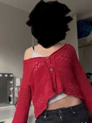Röd stickad cardigan med knappar - Cool röd stickad cardigan med knappar framtill och ett snyggt hålmönster. Tröjan är croppad och har långa ärmar, perfekt att slänga över ett linne. Materialet är mjukt och luftigt, vilket gör den bekväm att bära. Skriv gärna om ni har några funderingar eller om mer bilder 
