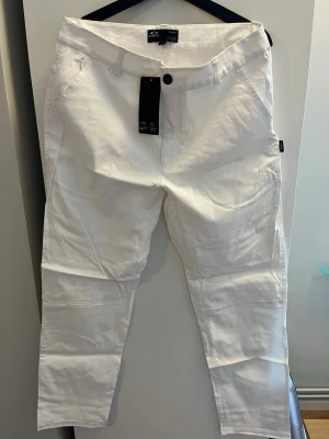 Vita regular fit byxor från Oakley - Snygga vita byxor från Oakley med regular fit och klassisk design. Byxorna har raka ben, knappstängning och sidofickor. Perfekta för dig som vill ha en clean och stilren look. Funkar som golfbyxa