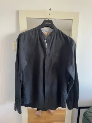 Springfield svart skjorta, storlek M - Säljer en mörkgrå henley-skjorta från McGordon med lång ärm och bröstficka. Skjortan har en klassisk knäppning vid halsen och är tillverkad i mjuk bomull. Perfekt för dig som gillar en enkel och stilren look.