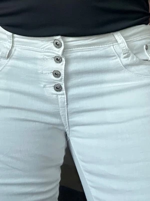 Vita skinny jeans med knappar - Säljer ett par vita skinny jeans med låg midja och fem synliga metallknappar framtill. Jeansen har klassiska fickor fram och bak och är i stretchigt material för en bekväm passform. Perfekta till en enkel topp eller hoodie.