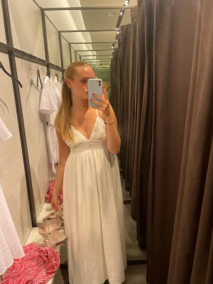 Vit lång sommarklänning - Säljer en vit lång klänning med smala axelband och v-ringning. Överdelen har fina virkade och kjolen faller luftigt ner. Perfekt för varma dagar och strandhäng. Dragkedja upptill, väldigt bra skick🩷
