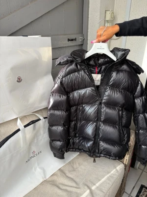 Svart dunjacka från Moncler - Säljer en svart, glansig dunjacka från Moncler. Köptes för cirka 1 år sen men endast använd 2 gånger. Nyskick!  Köptes i butik i Stockholm, kvitto finns med dustbag och taggar. Jackan är storlek 0 vilket motsvarar S. Skriv vid fler bilder eller frågor.❤️