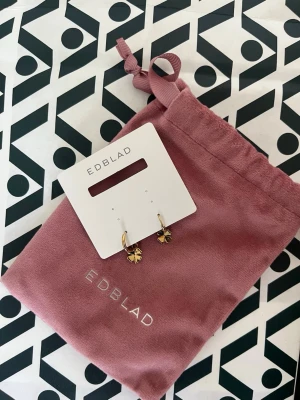  Edblad Lucky Hoops Gold - Snygga örhängen från Edblad. Guldpläterade hängande fyrklöverformade berlocker. Perfekta för dig som gillar stilrena och trendiga accessoarer med en touch av tur. Säljer p.g.a att använder inte guld smycken.💕