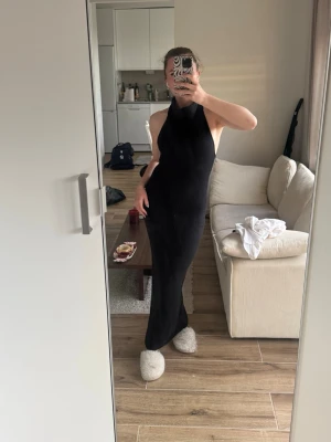 Svart lång stickad klänning - Säljer en svart långklänning i stickat material med halterneck och figurnära passform. Klänningen är ärmlös och har en enkel, stilren design som passar perfekt till olika tillfällen. Superbekväm och snygg att styla med accessoarer.