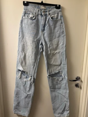 Ljusblå ripped jeans från Gina Tricot - Säljer ett par ljusblå jeans från Gina Tricot med raka ben och stora slitningar på båda knäna. Jeansen har klassisk femficksdesign och hög midja. Materialet är denim i bomull och de har en cool, avslappnad look.