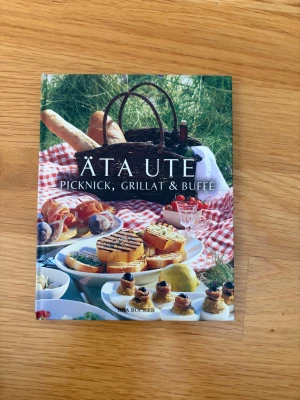 Äta ute: Picknick, Grillat & Buffé - En inspirerande bok med recept och tips för picknick, grillat och buffé. Färgglad framsida med matbilder och röd hård pärm. Perfekt för dig som vill laga mat utomhus och prova nya rätter.