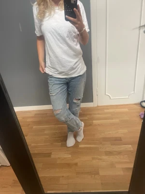 Ljusa slitna mom jeans - Säljer ett par ljusblå mom jeans med hål. Jeansen har raka ben och fransiga benslut för en avslappnad och trendig look. Perfekta för dig som gillar en casual och cool stil.