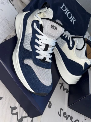 Skor b25 - Snygga sneakers  i blått och vitt . Skorna har snörning och är tillverkade i en mix av mesh och mocka för en modern look. Perfekta för dig som vill ha något exklusivt och trendigt i garderoben.